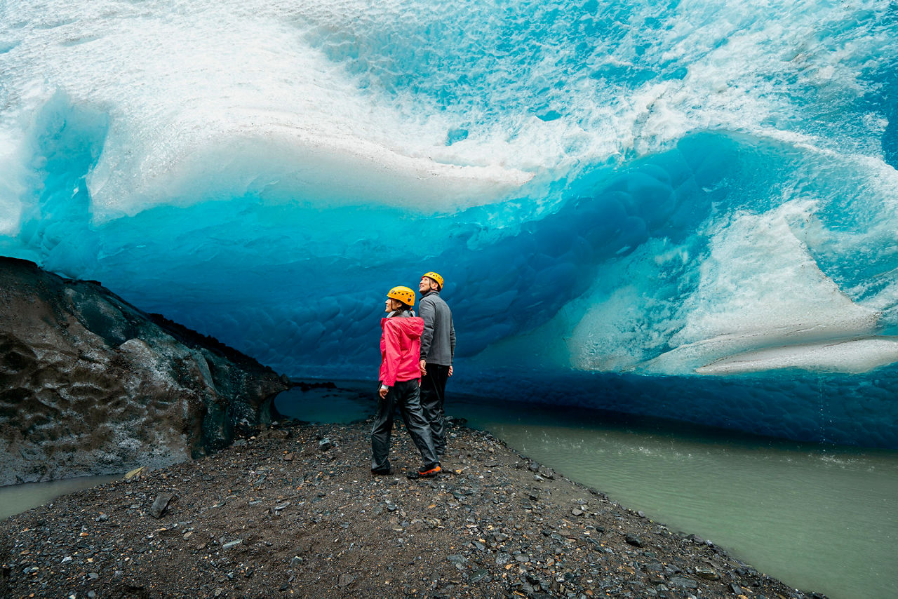 Couple standing on rocky area looking up into glacier, Alaska, Juneau