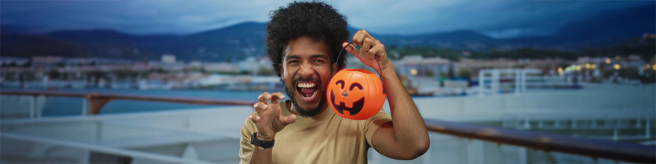 Man smiling and holding a halloween pumpkin basket on a cruise ship