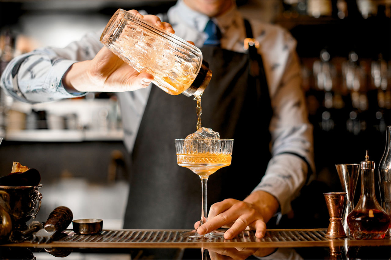 cocktail being poured from glass shaker into glass. North America.
