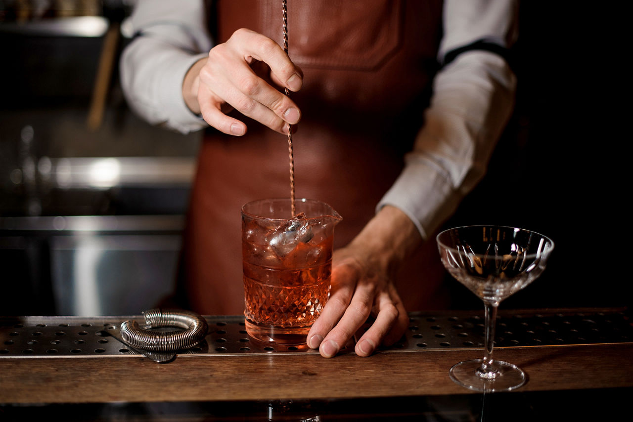 bartender mixing a red cocktail at speakeasy bar. North America.