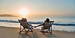 couple sitting in beach chairs on hold hands in front of a sunrise. The Caribbean.
