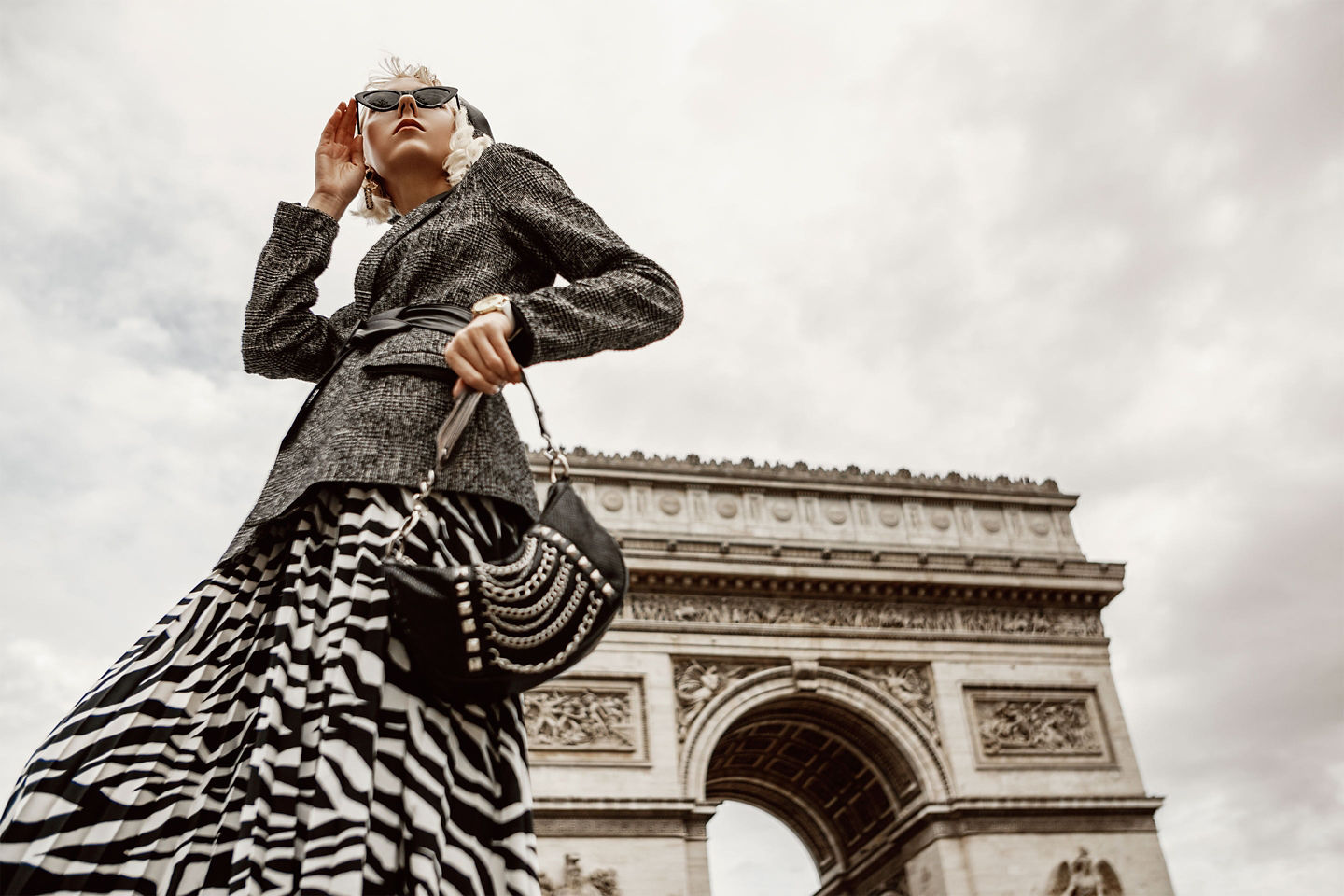 An elegant woman poses outdoors in autumn attire, blending warm tones with a refined, luxe style. - Paris, France