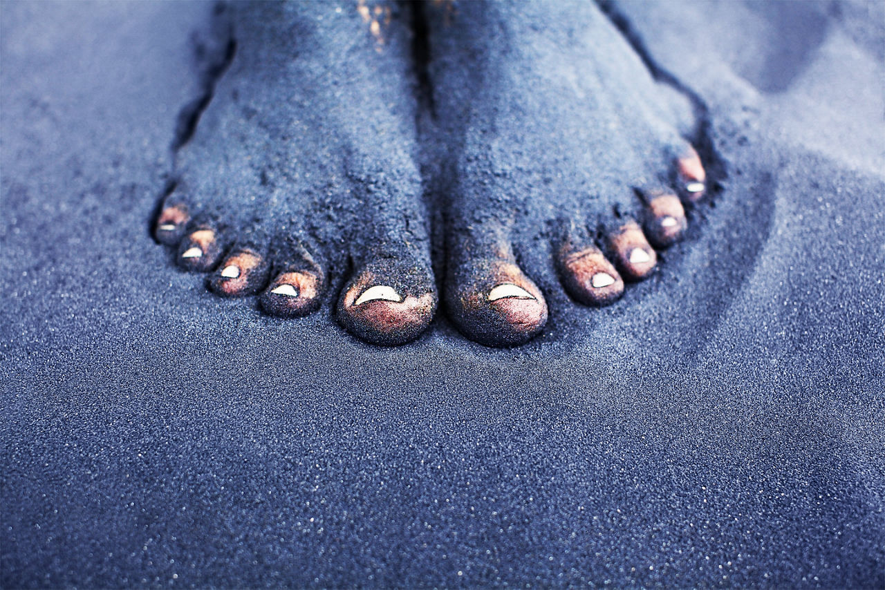 feet covered in sand on a volcanic beach vacation. The Caribbean.