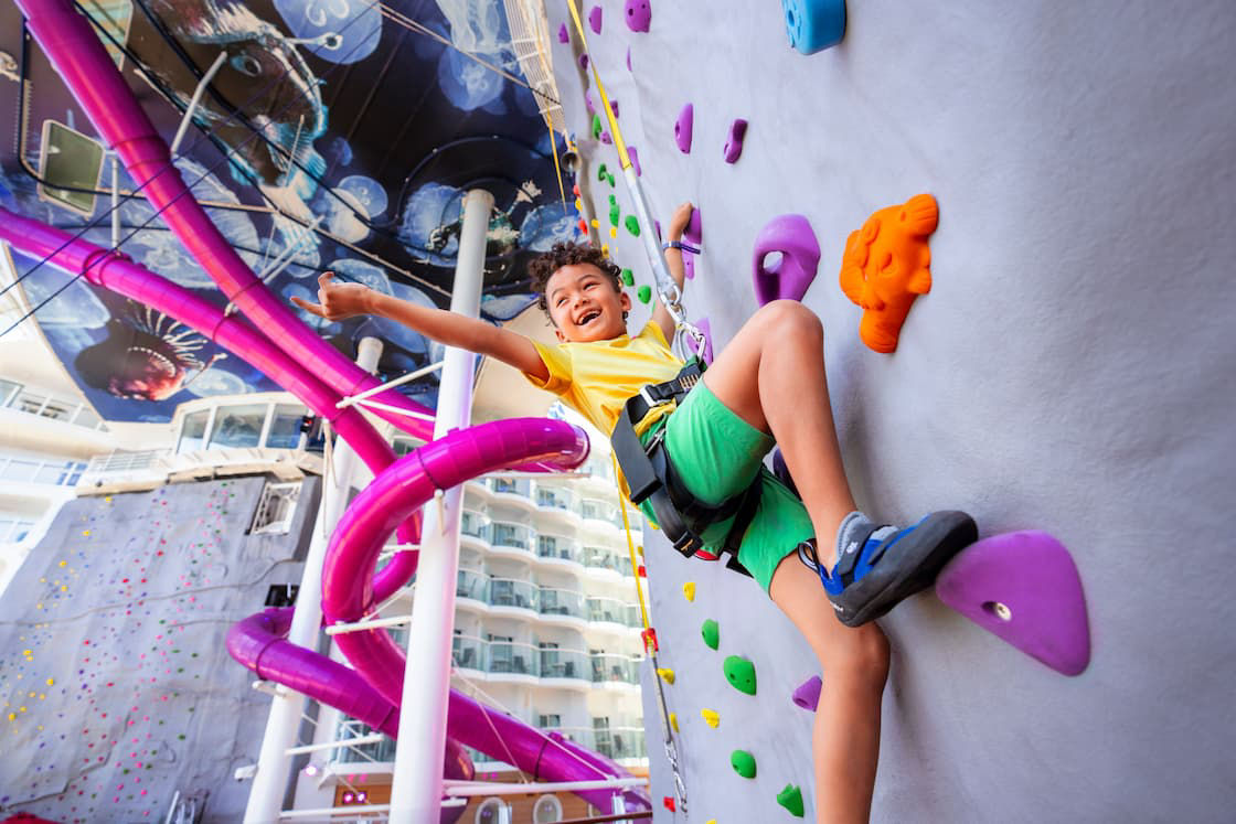 Young boy happy climbing rock wall while pointing