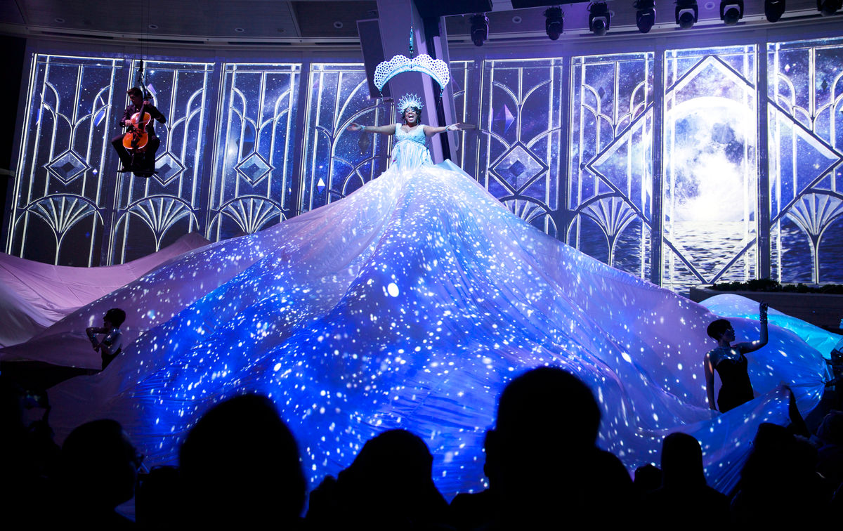 Singer on stage wearing a huge dress skirt that glows blue during Starwater acrobat show on Quantum.