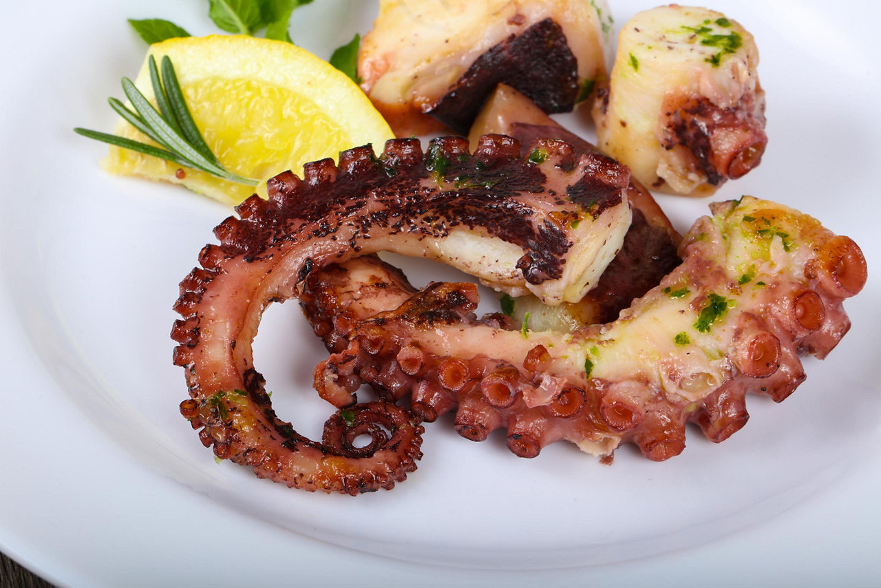 Grilled octopus on a white plate with a lemon on the side