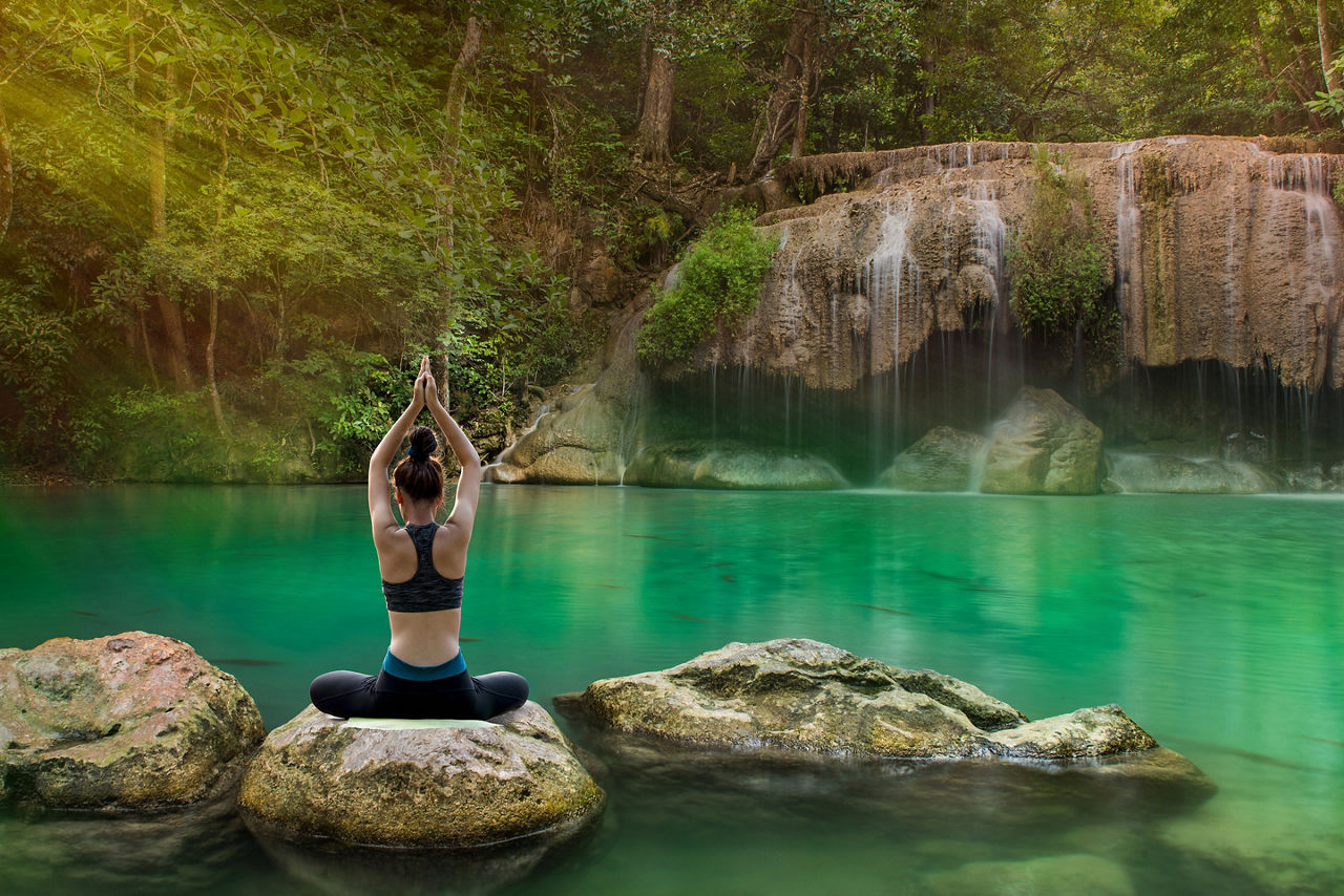 Woman practicing yoga on the rock in waterfall on the mountain