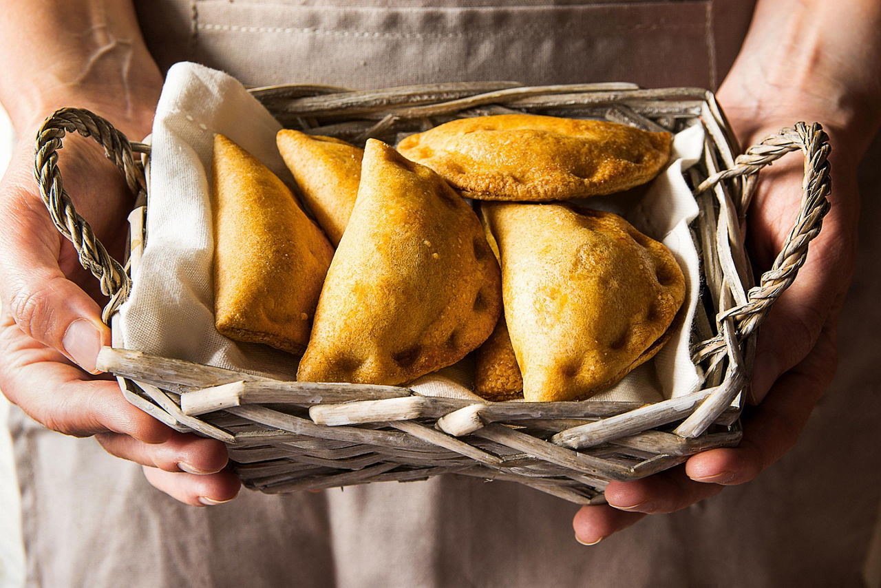 Young woman holding in hands wicker basket with freshly baked empanadas