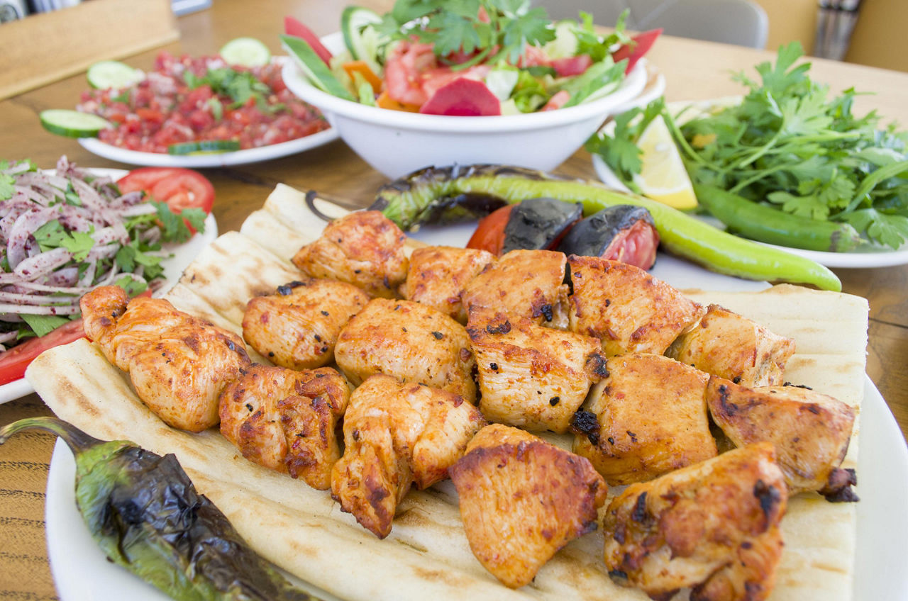 Multiple chicken shish kebobs with a bowl of salad on the side