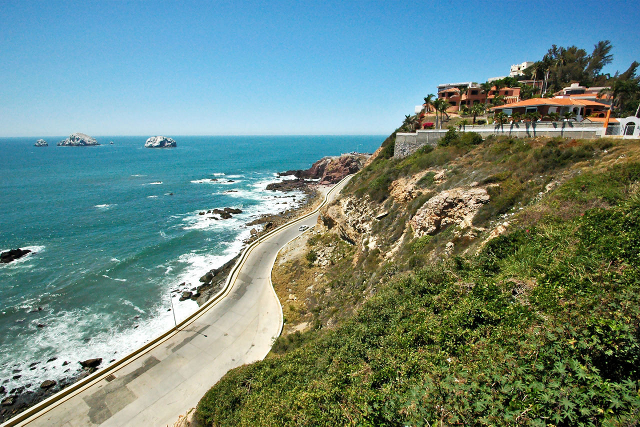 Colorful city sits atop a hill next to the ocean with road below in Mazatlan. Mexico.