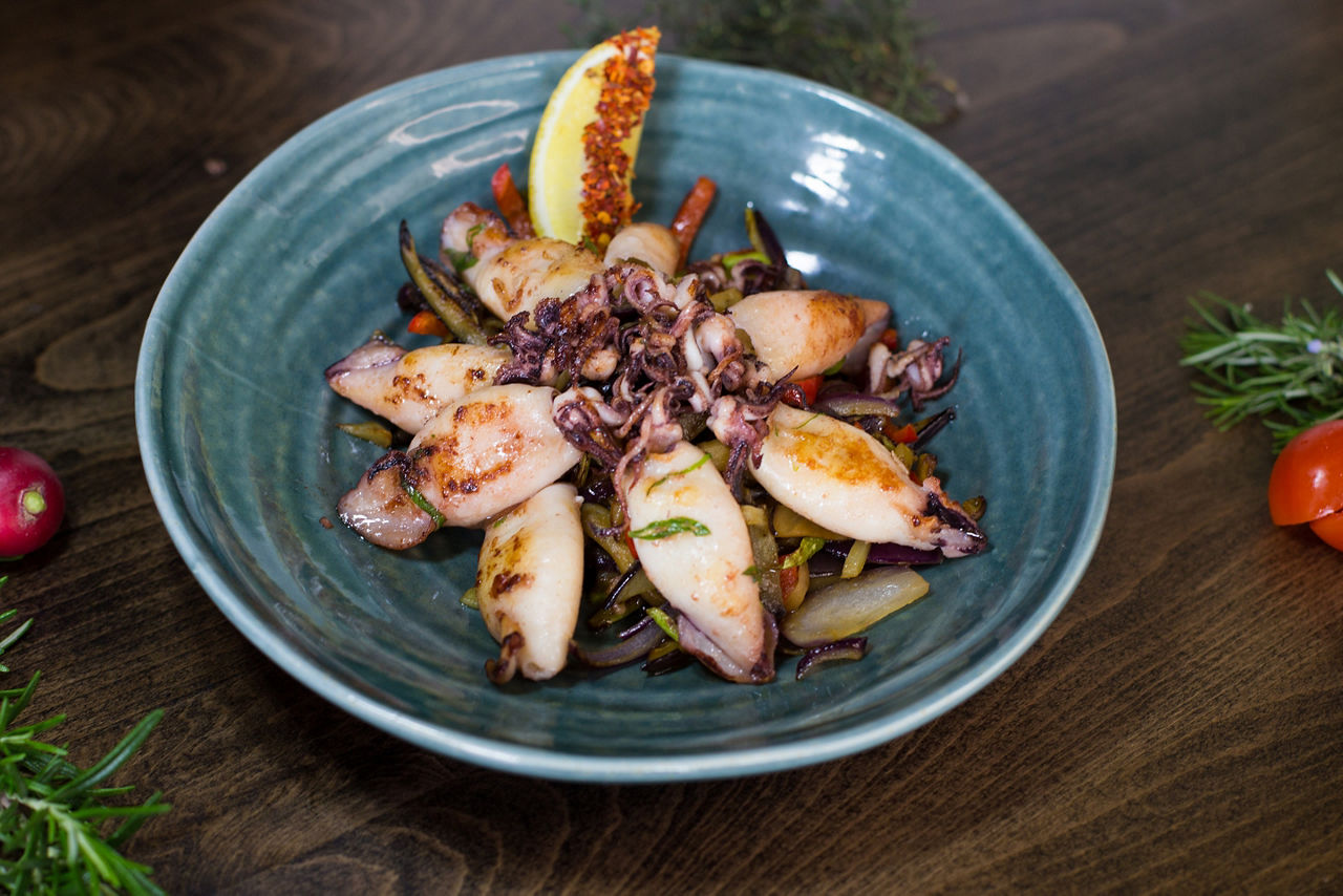 Fried patagonia squid on a pillow of vegetables on a blue plate, on a wooden table