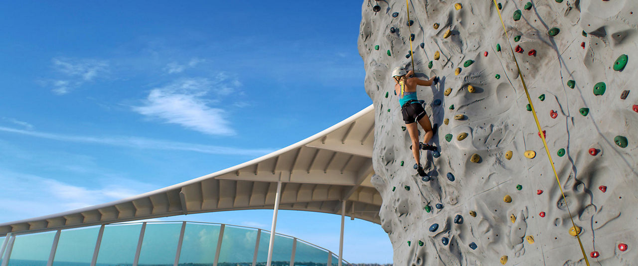 Woman Climbing Rock Wall Enjoying Ocean Views