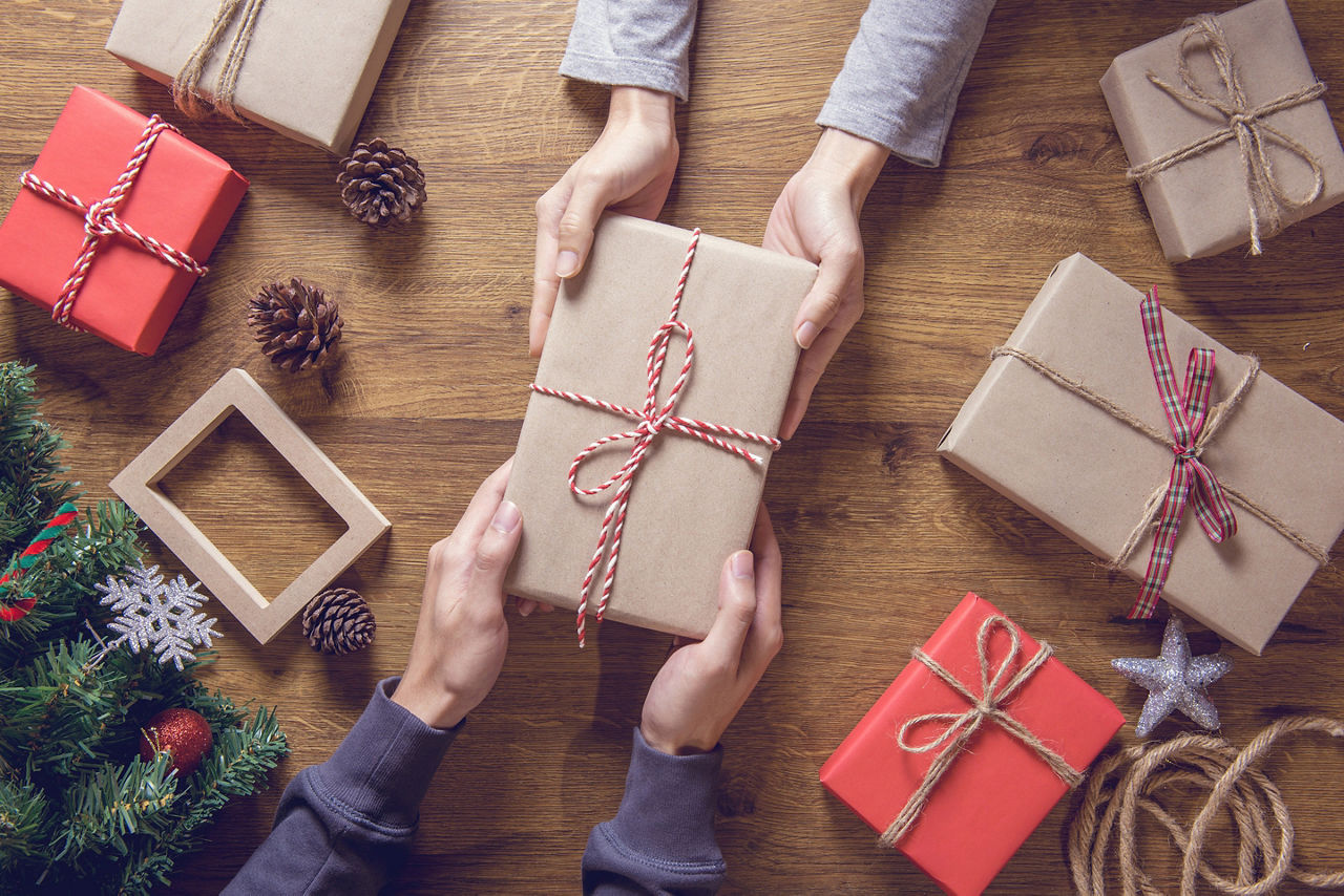 Two Holiday Volunteers Pass a Wrapped Gift to Each Other Across the Table