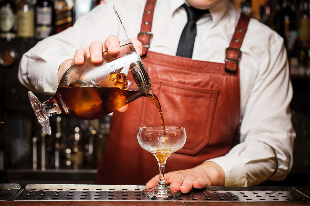 bartender pours a cocktail at an upscale speakeasy bar. North America.