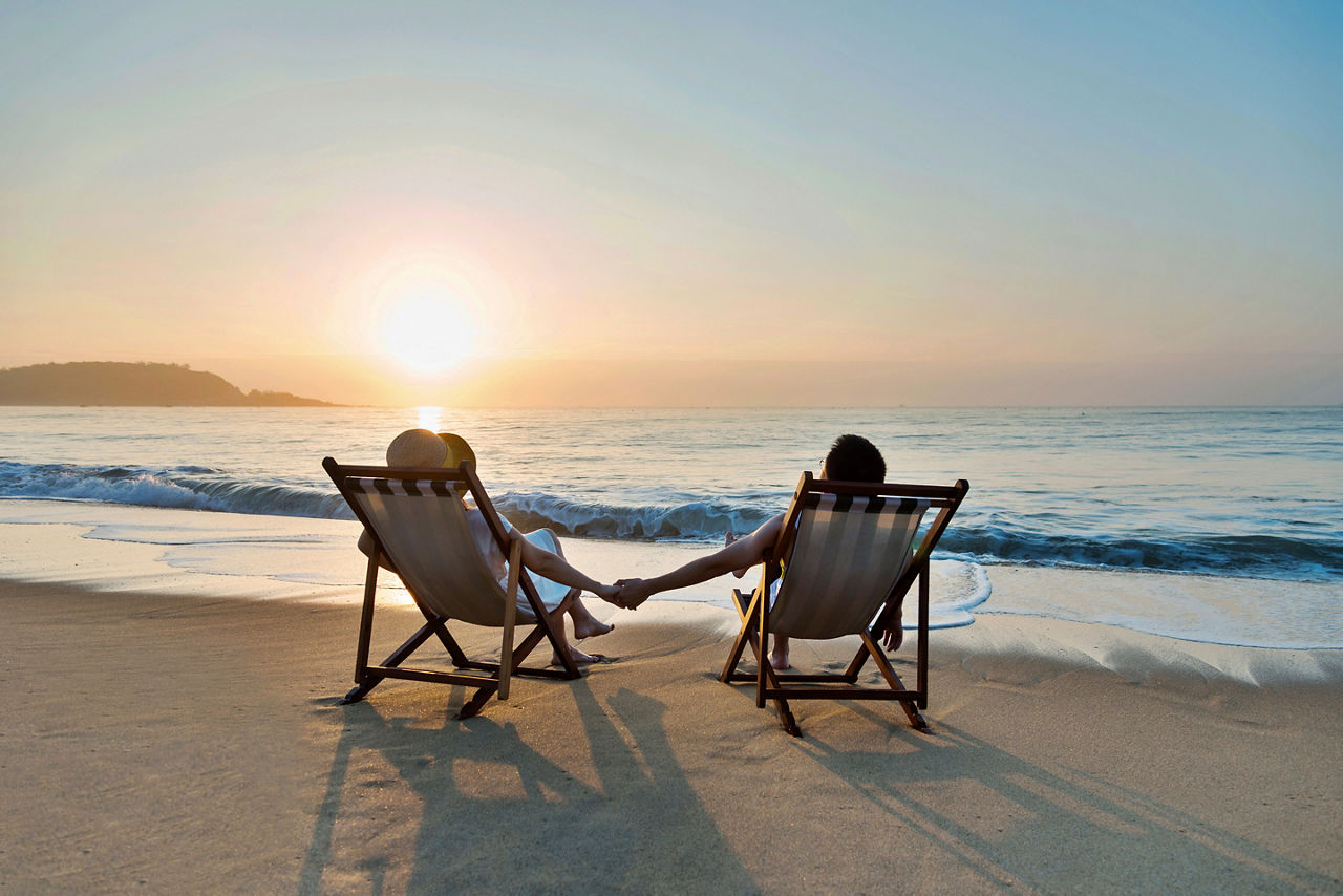 couple sitting in beach chairs on hold hands in front of a sunrise. The Caribbean.