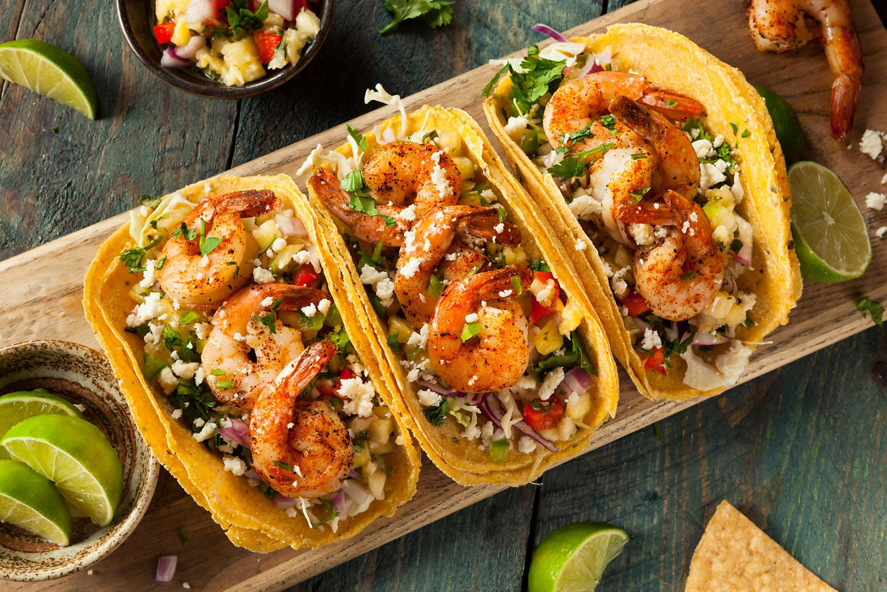 Three shrimp tacos with coleslaw and salsa on a wooden board