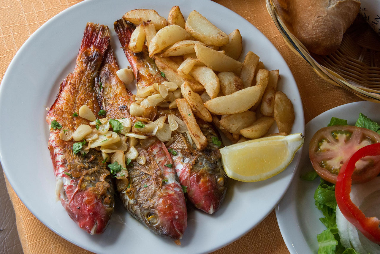 Three whole grilled fish with potatoes and salad on a white plate