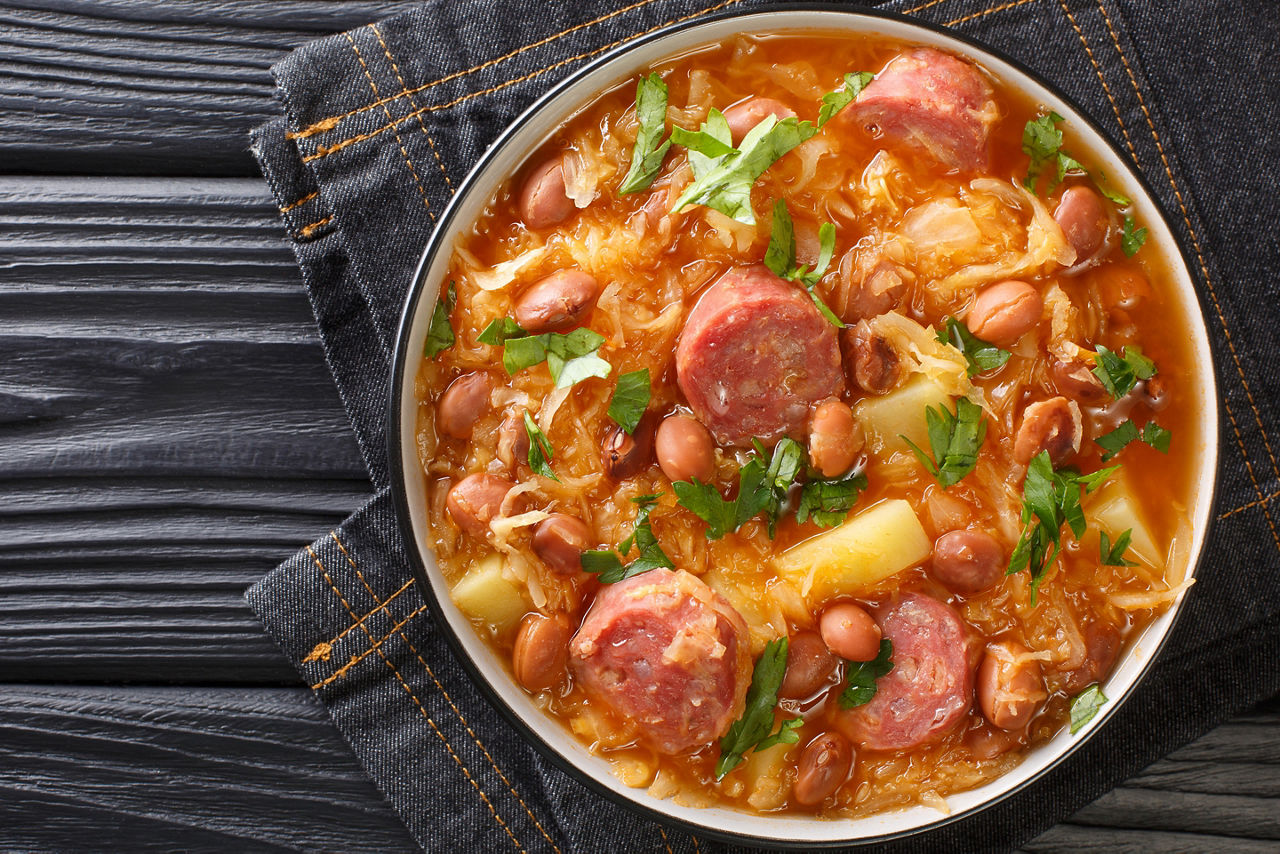 Jota Sauerkraut stew with borlotti beans, potatoes and sausages close-up in a bowl on the table. 