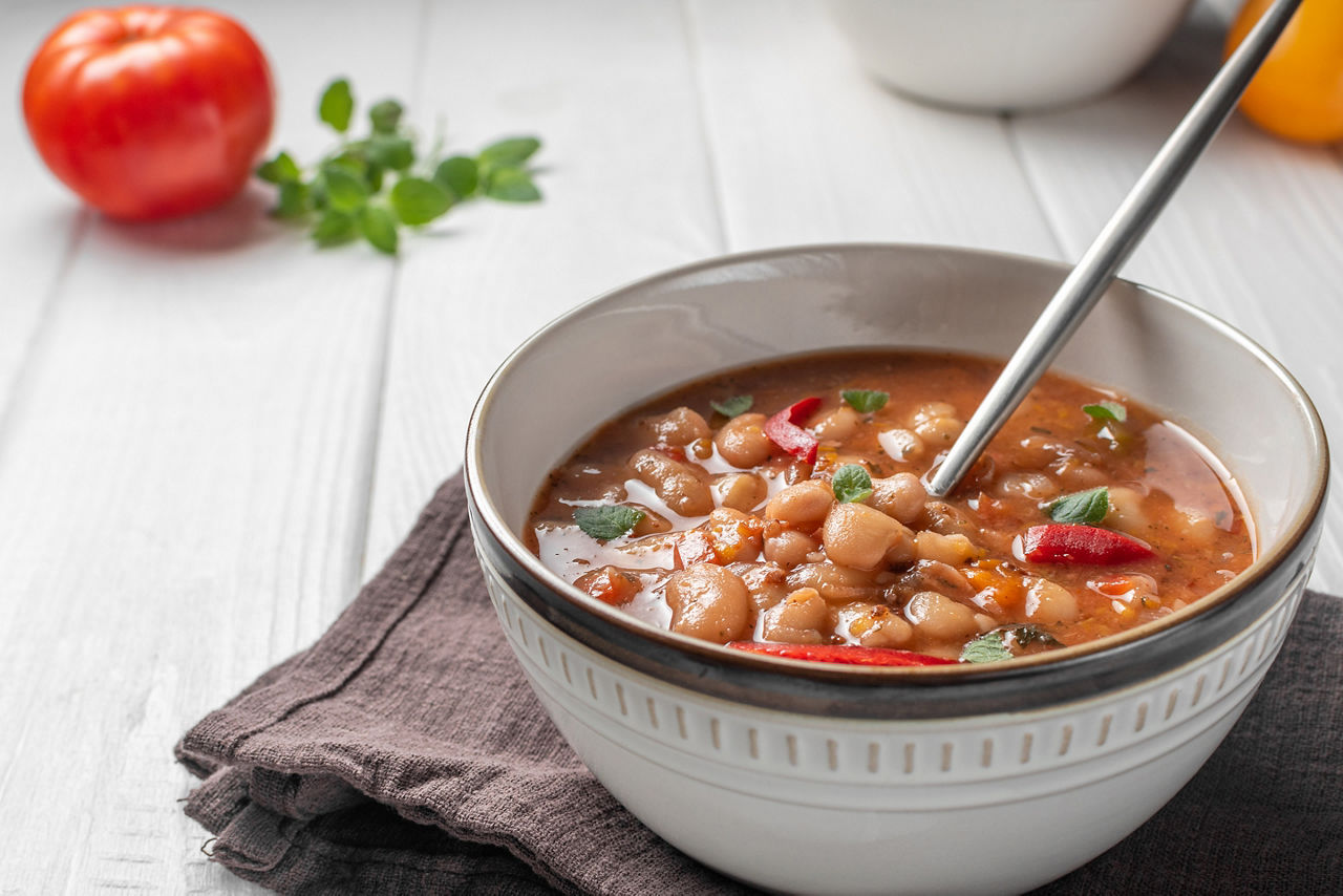 Bulgarian Soup Bob Chorba whith been, tomatoes, bread and mint on white wooden table. 